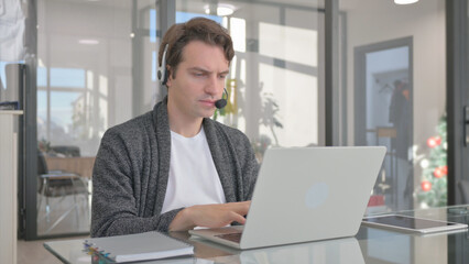 Fototapeta premium Young Man with Headset in Call Center Working on Laptop