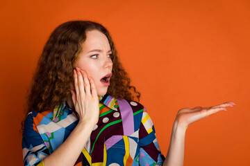 Photo of astonished shocked pretty girl wear trendy print clothes hold look news empty space isolated on vivid orange color background