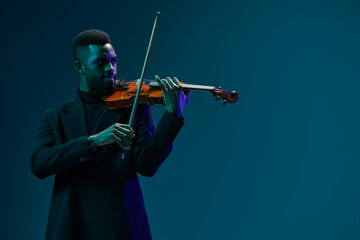 African American man in black suit playing violin on blue background creating a soulful melody