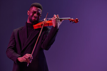 Professional violinist in black suit playing classical music on violin against purple background concert performance art musician portrait © SHOTPRIME STUDIO