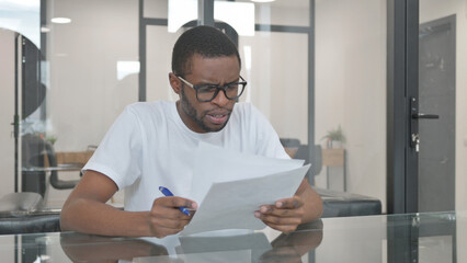 Young African Man Reading Documents at Work
