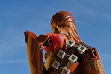 Naklejka premium LEGO Star Wars large action figure of Wookie Chewbacca, also called Chewie, eating slice of red salami, blue skies with some clouds in background. 