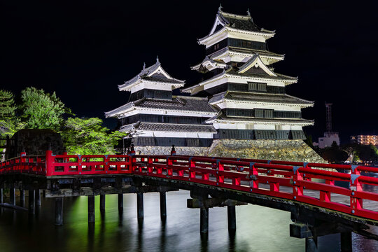 Japanese Matsumoto Castle and red bridge reflected in its moat at night