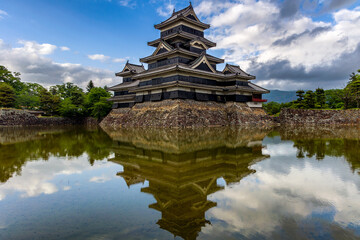 Ancient Japanese castle reflected in its moat with a blue sky behind (Matsumoto)