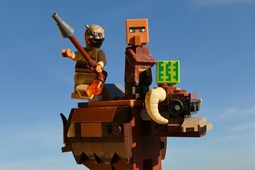 Fototapeta premium LEGO Tusken raider and Minecraft villager with square watermelon riding on Banthas bull mount, clear spring blue skies in background. 