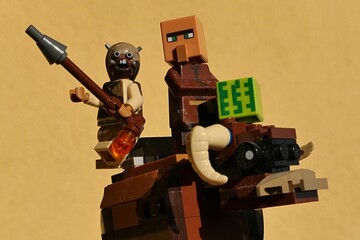 Fototapeta premium LEGO Tusken raider with his rifle and Minecraft villager with square watermelon riding on Banthas bull mount, yellow wall in background. 