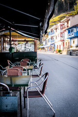 Restaurant terrace in Lastres, Asturias, empty tables and chairs, sunny village street.