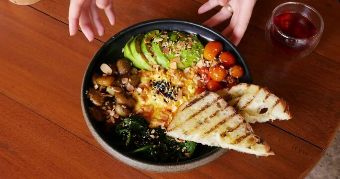 Woman waiter puts plate with large and nutritious breakfast on table. A juicy looking and beautiful dish served at popular restaurant in Bali. Close view of food, only hands of woman in frame