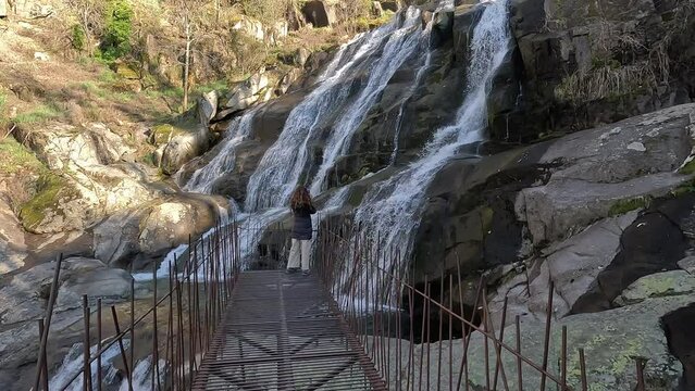 Woman with her back on a walkway taking a photo of the beautiful Caozo Waterfall in the Jerte Valley, in Caceres, Extremadura, Spain
