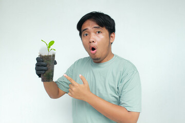 A young Asian man holds a vegetable plant pot made from used plastic bottles with an amazed...