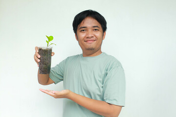 A young Asian man holds a vegetable plant pot made from used plastic bottles with an happy...