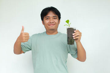 A young Asian man holds a vegetable plant pot made from used plastic bottles with an happy...