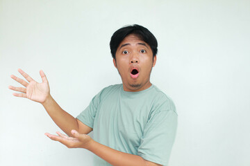 Young asian man in green t-shirt with wow expression. While pointing left. Isolated on gray background.