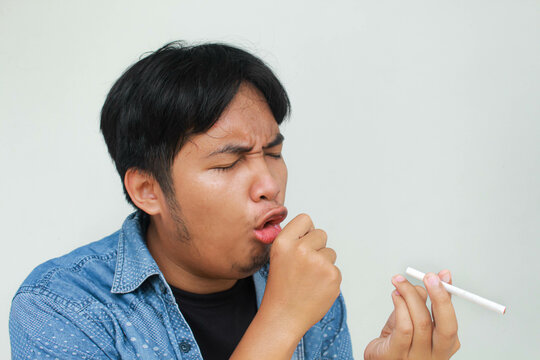 Smoker holding a cigarette suffering from chronic cough, Asian man patient coughing with respiratory problems, emphysema disease or lung cancer from smoking, medical and health care concept.