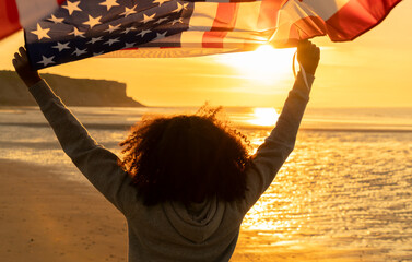 African American Girl Teenager Holding an American US Flag on a Beach at Sunset - 777419044