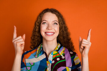 Photo of cheerful satisfied girl wear trendy print clothes look up empty space isolated on vibrant orange color background