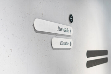Gray concrete wall with directional signs indicating men's toilet and elevator