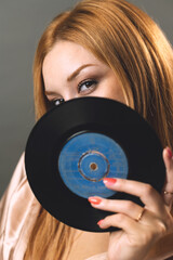 A young woman gazes through the center of a vinyl record, merging fashion with music nostalgia - 777426896