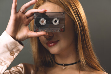 A young woman creatively obscures her eyes with a vintage music cassette tape - 777427411