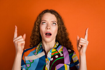 Photo of charming astonished girl wear stylish print clothes presents empty space isolated on vibrant orange color background