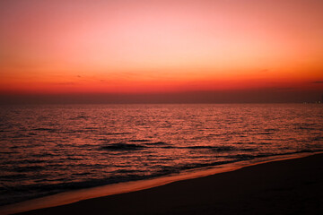 Obraz premium The sea after sunset has an orange glow and an orange sky with no clouds.