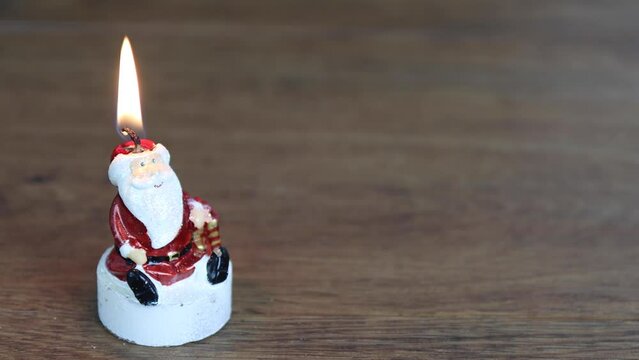 A Christmas candle in the shape of Santa Claus on a wooden background being lit by a lighter then blown back out