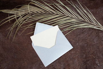 Gray blank postcard with a silver envelope,  and a dried palm leaf on genuine leather background,   invitation concept