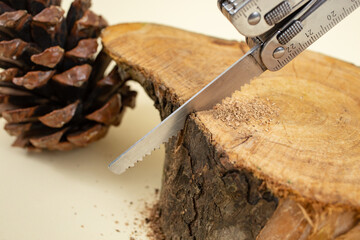 Swiss army pocket knife sawing a wooden log on beige background, soft focus close up
