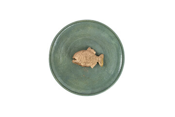 Golden piranha fish painted on a green ceramic plate, isolated on white background, abstract concept
