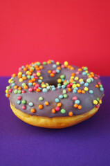 Donut with lilac glaze and sprinkles  on pink and purple background