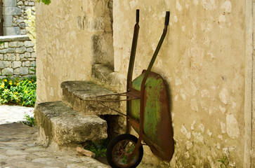 Old rusty common wheelbarrow is positioned against a stone building in front of a stairway in...