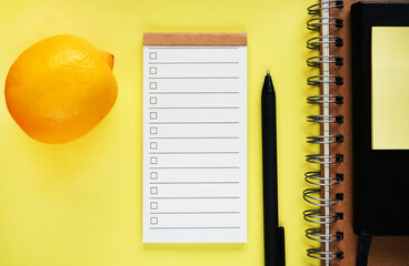 To-do list next to lemon, notepads and pen on yellow background