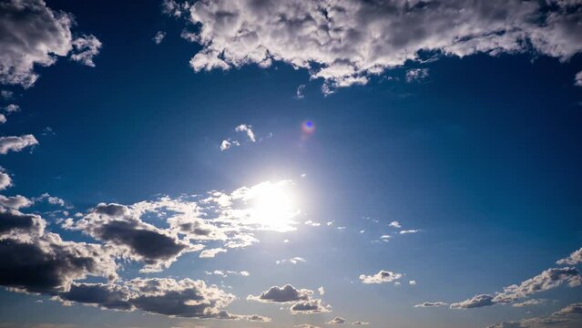 Timelapse of cumulus clouds moving in the blue sky against the sun. Cloud space background with many light and grey clouds changing shape, time lapse. Change of weather. Nature, sky clouds, copy space