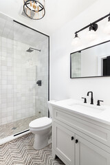 A bathroom with a white cabinet and countertop, black and gold light fixtures, and a stripe tile...