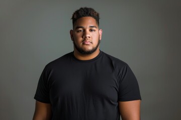 Obraz premium A studio portrait of a plus sized young man with a confident expression, wearing a plain black t-shirt. Ideal for fashion branding and body positivity campaigns.