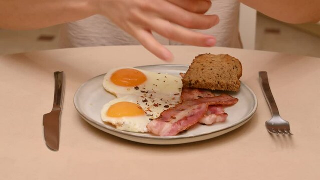 A woman puts too much pepper on her bacon and eggs. Exaggeration on the topic of excessive consumption of spicy food