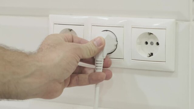 man inserts  plug into an electrical outlet, slow motion, selective focus
