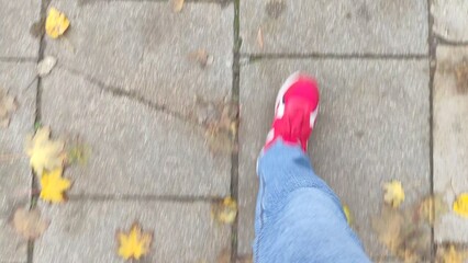 Man walks on paving slabs with fallen leaves. First person view