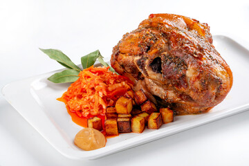 Pork knuckle baked in the oven in a plate with stewed cabbage and potatoes on a white background. Bavarian meat dish