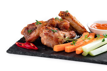 Grilled chicken pieces on a slate board with fresh vegetables and sauce isolated on white