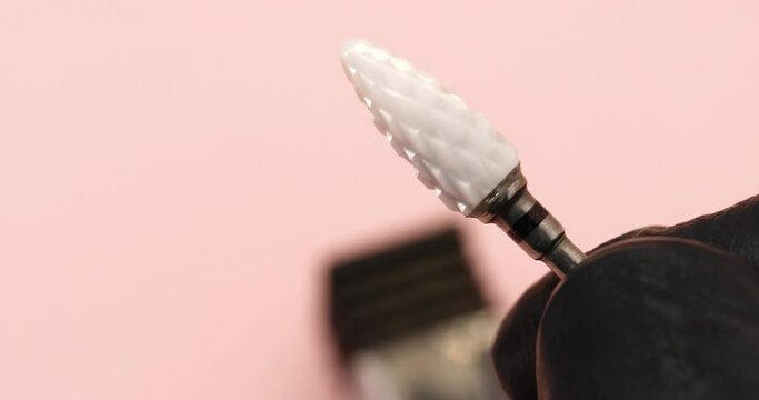 A specialist in gloves holds in his hand a ceramic cutter for hardware manicure with a black notch for removing gel polish with copy space on a pink background