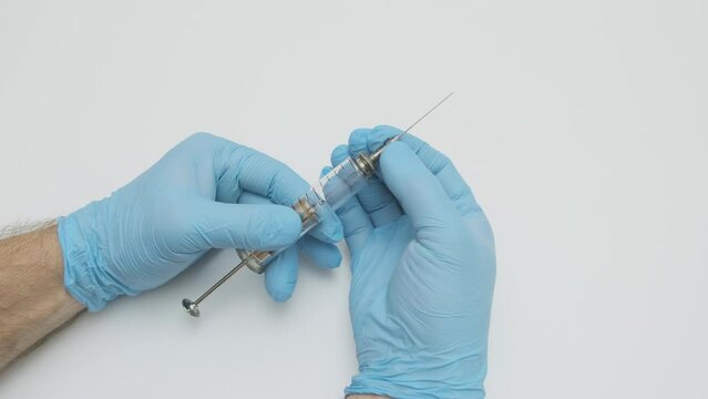 doctor in blue medical gloves puts metal needle on old glass syringe, slow motion, selective focus
