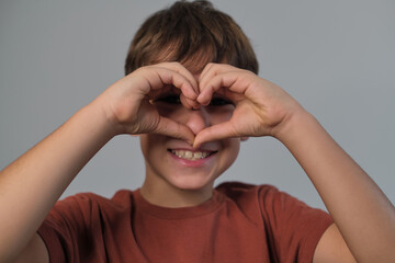 Boy in a terra-cotta shirt forms a heart with his fingers, smiling sweetly. A beautiful reminder of the innocence and pure affection in childhood.