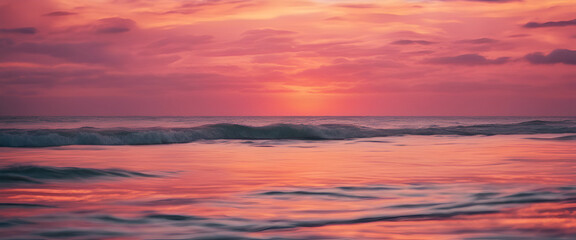 A pink sunset over the ocean, with waves gently lapping at shore and a distant sun setting behind...