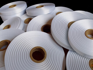 pile of rolls of white ribbon on black background. a collection of thick satin ribbons with rough...