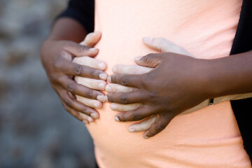 White man hugging pregnant black woman. Le Mesnil en Ouche, France. Close-up on hands and belly