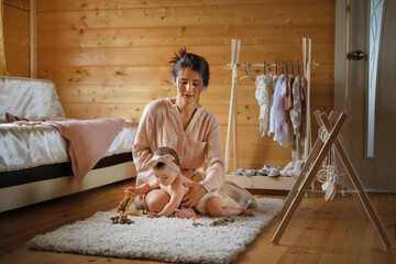 Careful hands guide a baby into clothes, amidst a rustic room. This picture celebrates the intimacy of a mother's touch.