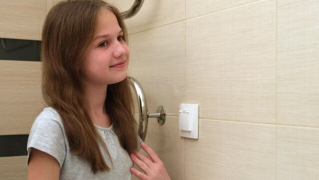 Preteen girl checking her face and hair in mirror. Caucasian smiling girl looking at her mirror reflection at home