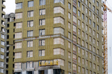 High-rise under construction with yellow insulation and exposed framework, next to a crane