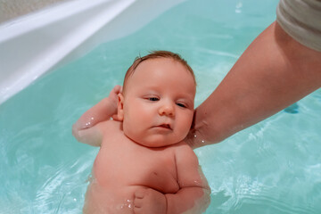 Fototapeta na wymiar A baby seated in a pool of water is being held securely by an individual